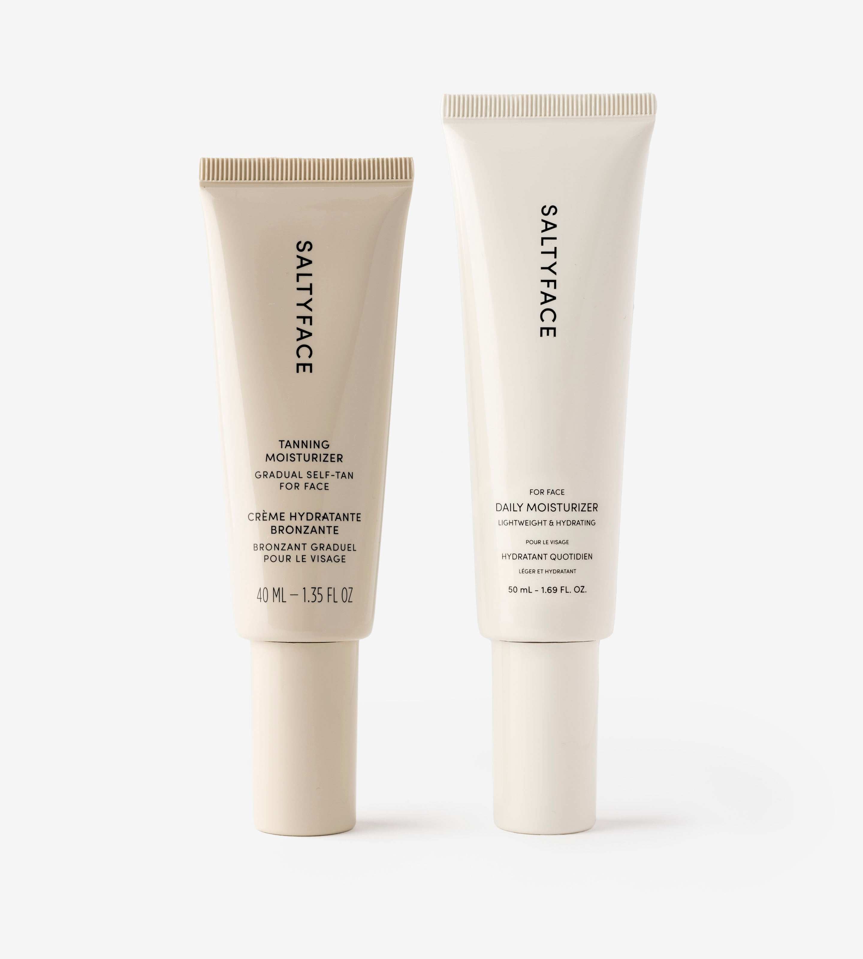 The Moisturizer Duo by SALTYFACE features two upright tubes—Tanning Moisturizer and Daily Moisturizer—on a white background, offering hydrated, glowing summer skin with their sleek minimalist black-on-white design.