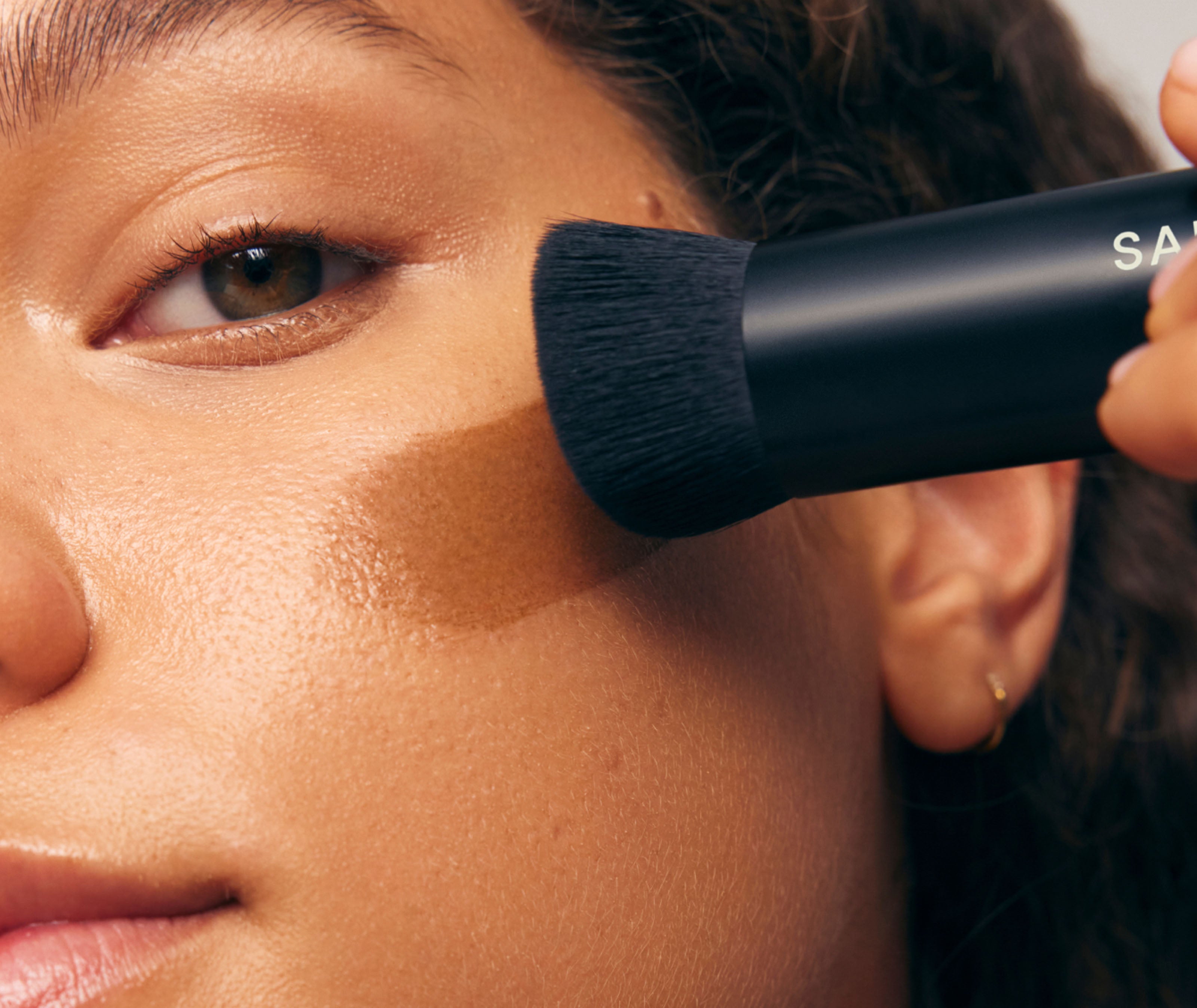 Person applying makeup with a brush, focusing on the face.
