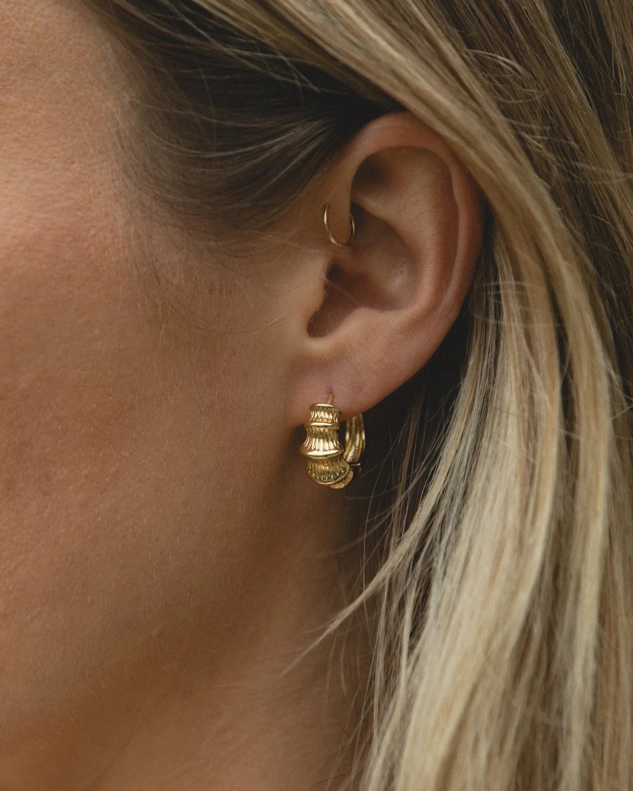 Close-up of a person wearing gold hoop earrings with blonde hair.